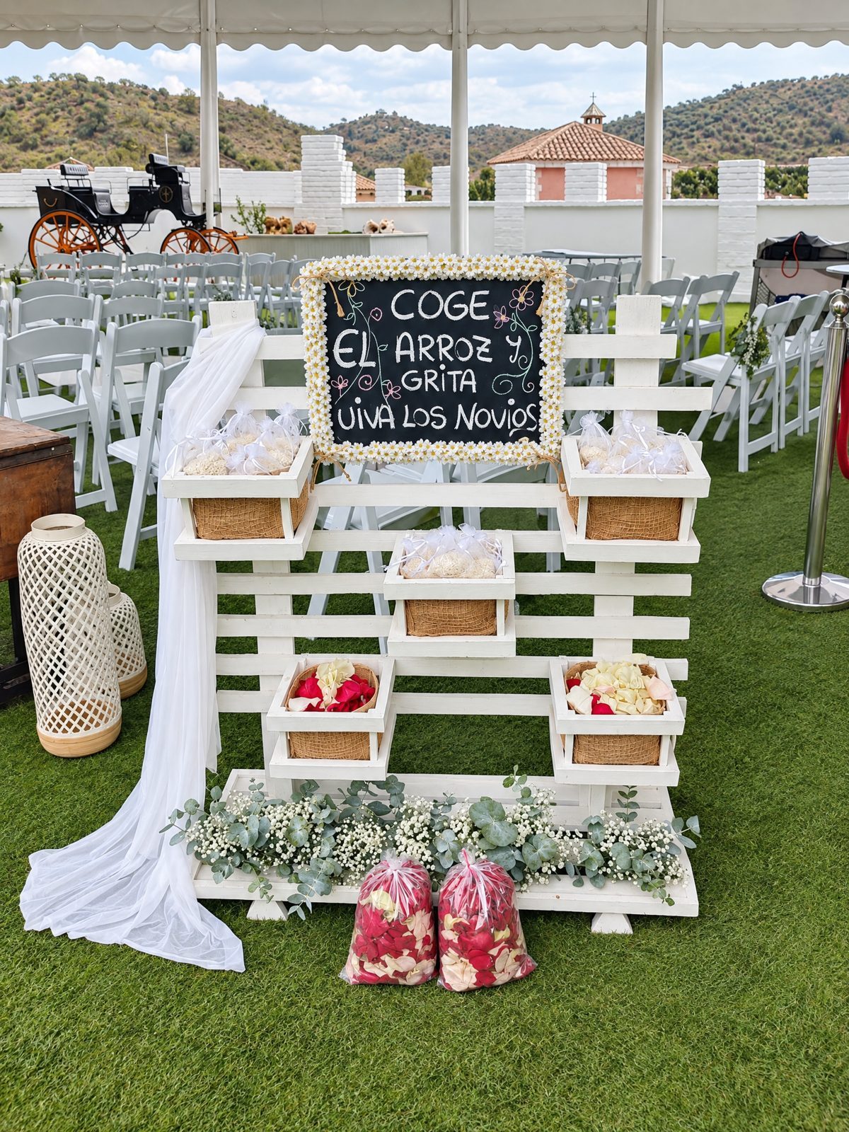 White wooden stand with baskets and a chalkboard saying «Take the rice and cheer for the newlyweds»