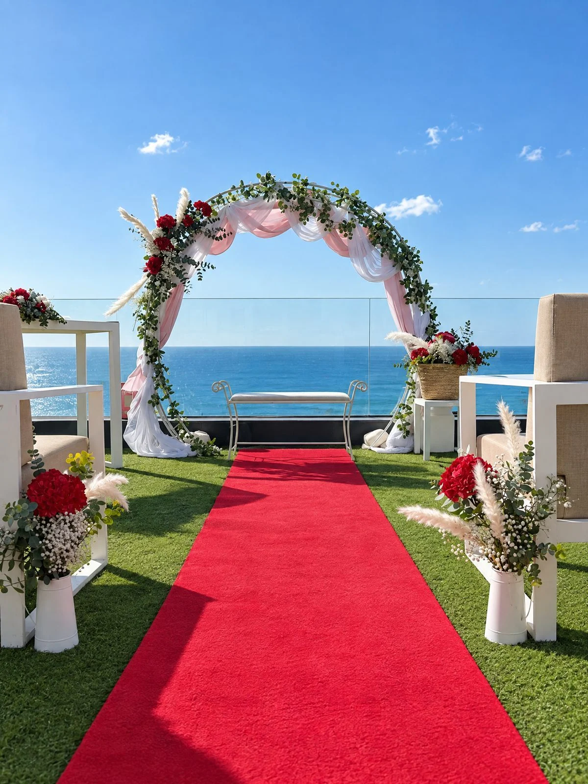 Wedding arch with red roses and tulle at the end of a red aisle runner, on a seaside terrace