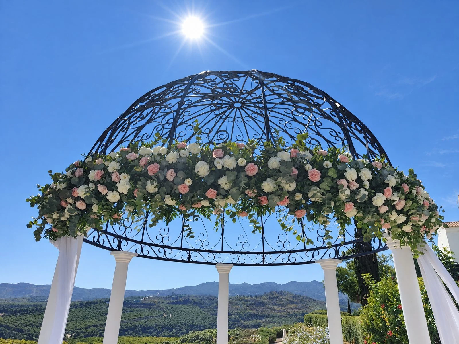 Wrought-iron gazebo with a flower garland and the mountains behind